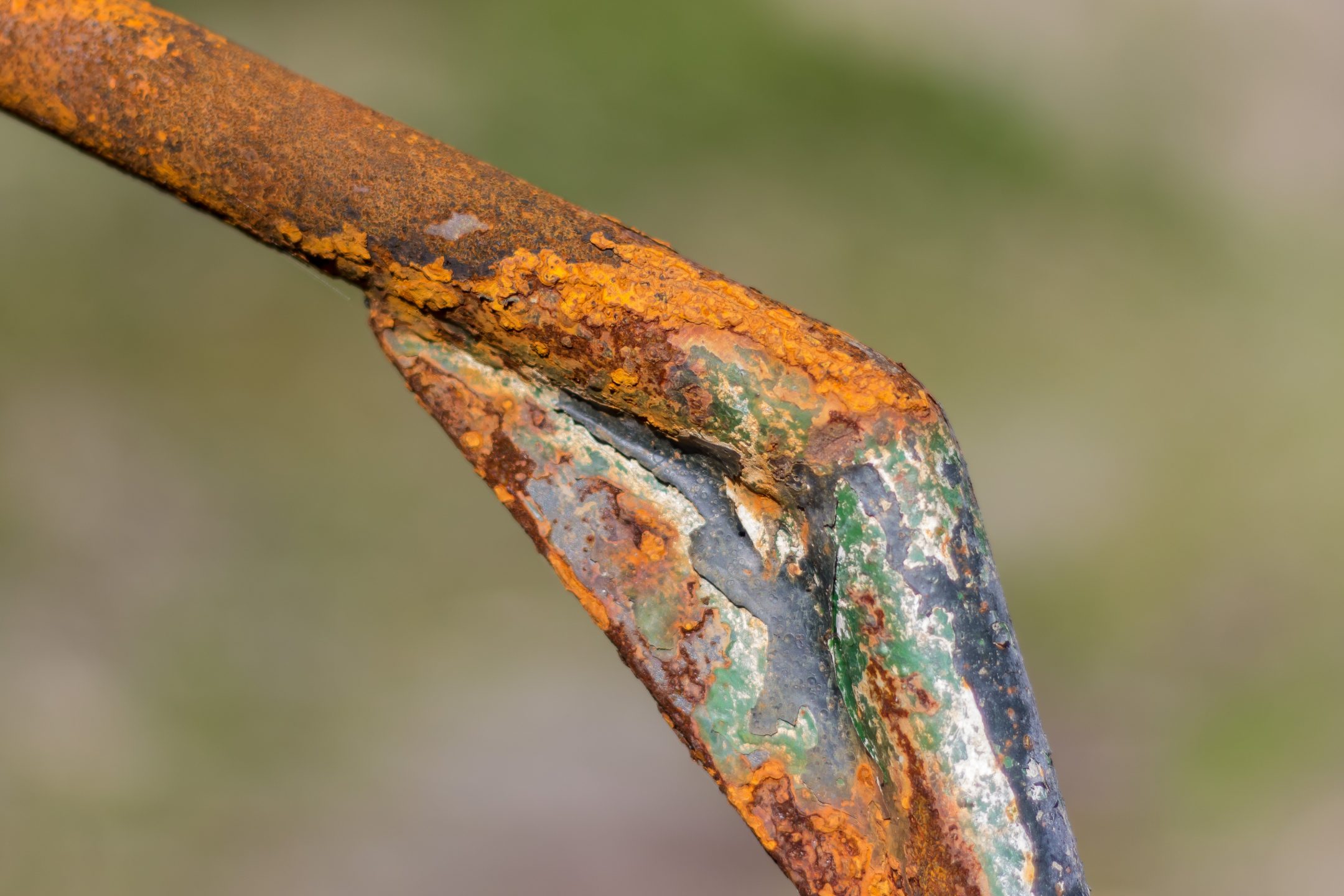a metal rode has green and orange oxidation against a blurry background